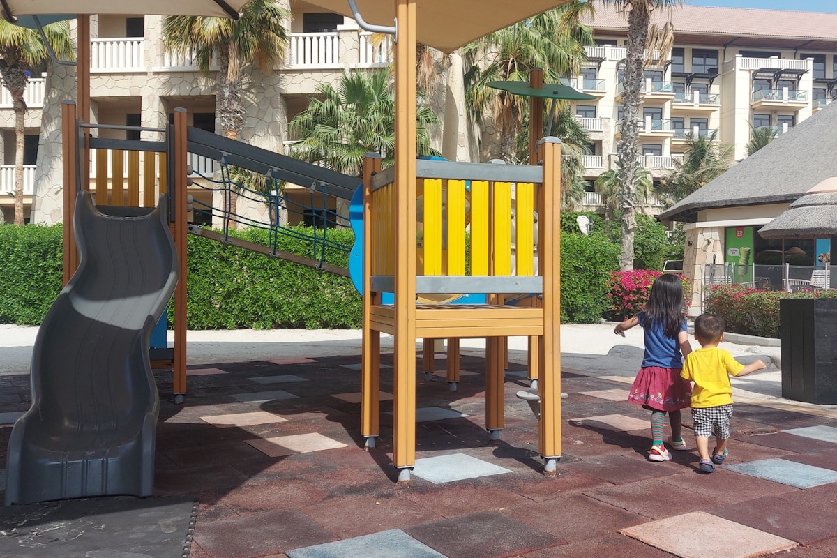 Two children walking hand-in-hand near a colorful playground with a slide and climbing structure