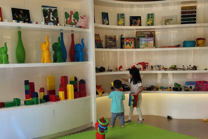 Two children exploring a colorful playroom filled with shelves of toys, games, and decorative figures.