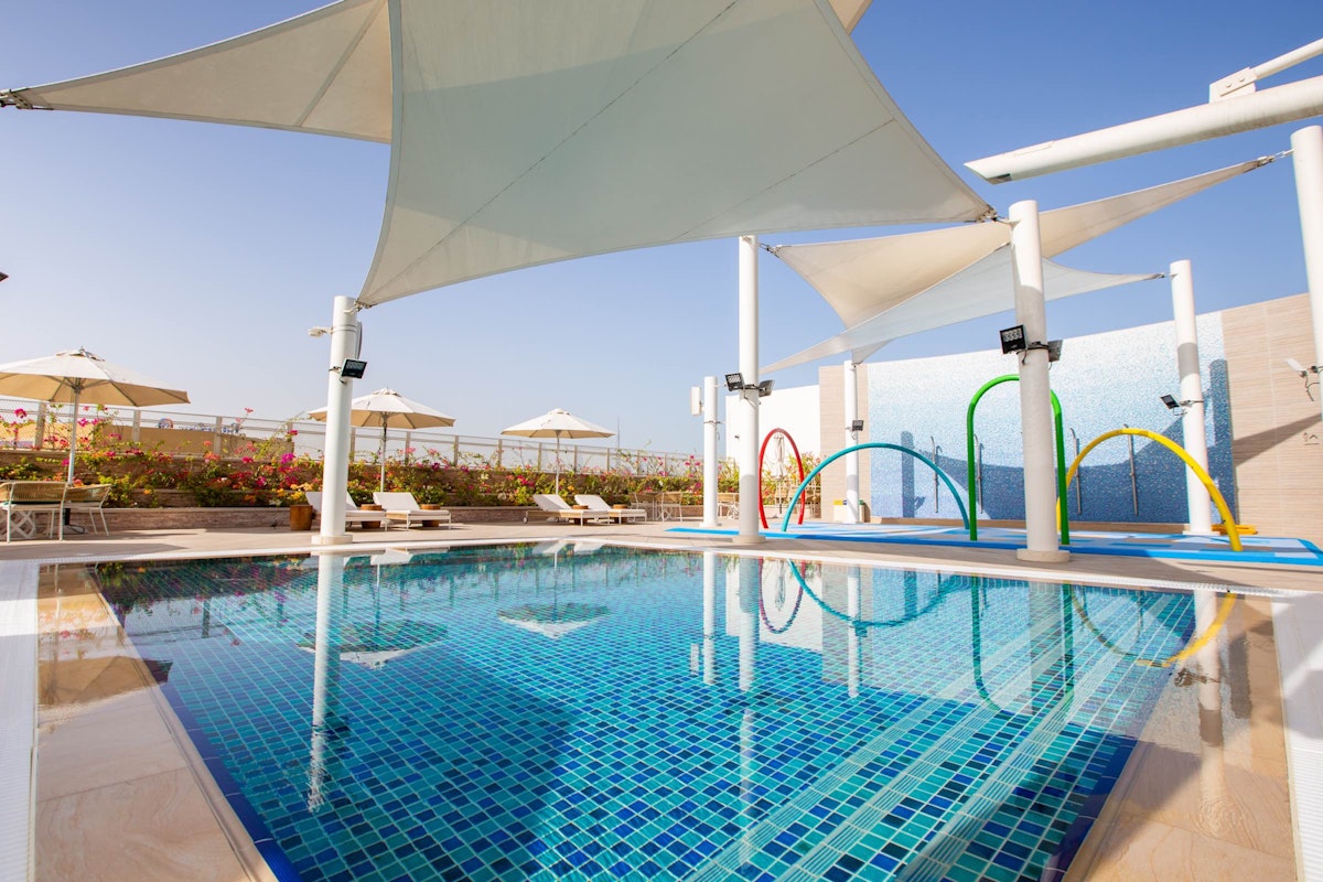 Sofitel Dubai The Obelisk Children's splash pool with water play equipment and colorful water jets, surrounded by umbrellas and a sunny sky.