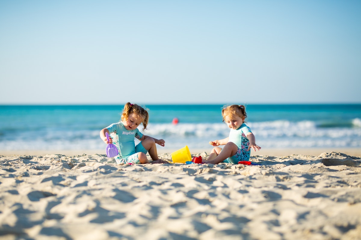 Two young children playing with toys on a sandy beach