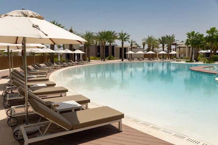 Sunbeds with umbrellas around a pristine swimming pool, surrounded by palm trees.
