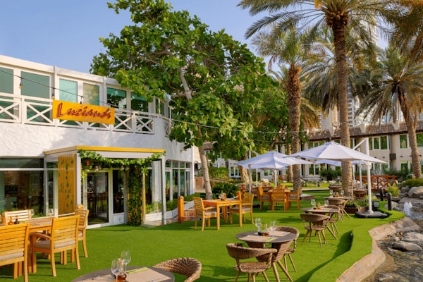 Outdoor restaurant seating with tables under umbrellas surrounded by lush greenery and palm trees
