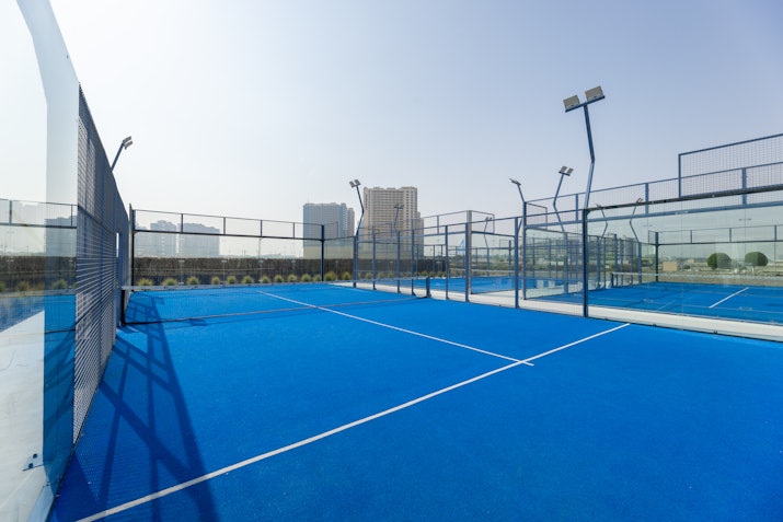 Empty paddle tennis court with blue flooring and fencing.