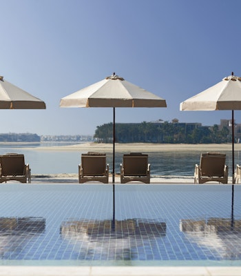 Waldorf Astoria Dubai Palm Jumeirah Three poolside loungers with umbrellas overlooking calm waterfront.