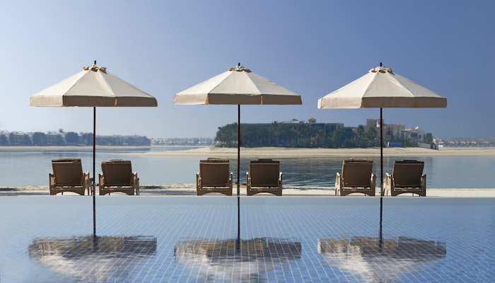 Waldorf Astoria Dubai Palm Jumeirah Three poolside loungers with umbrellas overlooking calm waterfront.