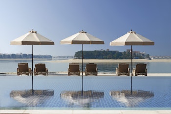 Three poolside loungers with umbrellas overlooking calm waterfront.