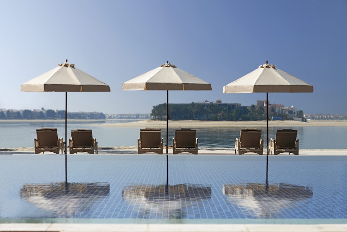 Three poolside loungers with umbrellas overlooking calm waterfront.