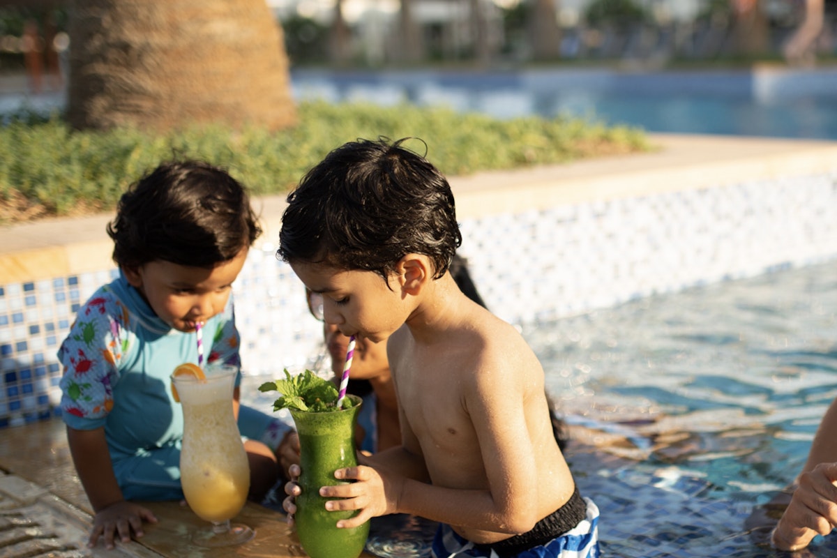 Privilee After School Hangouts Two children enjoying drinks by the pool, with one holding a green drink and the other a yellow one.