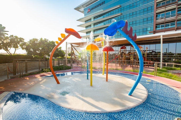 Marriott Hotel Al Forsan A colorful water play area with spray fountains, set against a modern building backdrop.