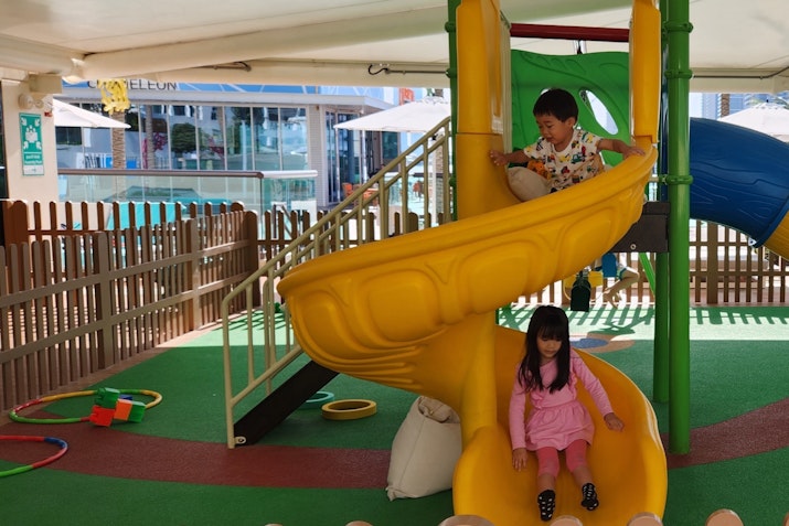 Two children playing on a colorful playground slide, with one child sliding down and the other sitting at the top.