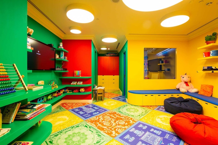 rightly colored playroom with green and yellow walls, featuring a TV, colorful bean bags, and shelves filled with toys and books