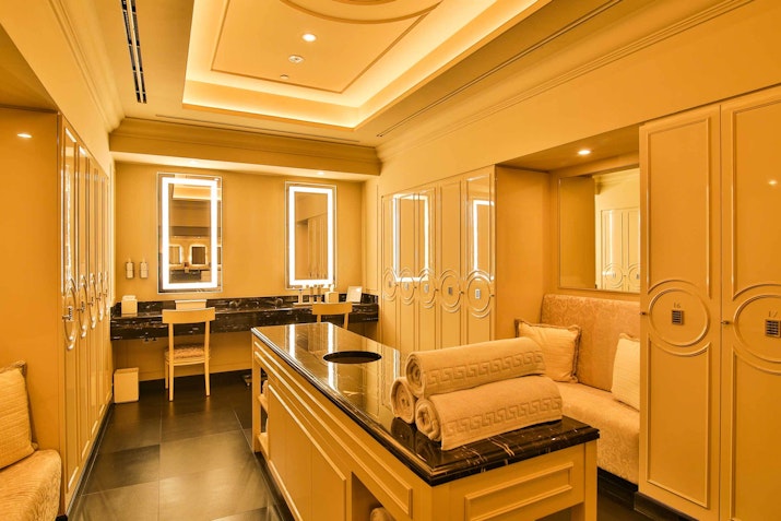 Luxurious spa room with golden decor, featuring mirrors, seating, and neatly rolled towels on a counter.