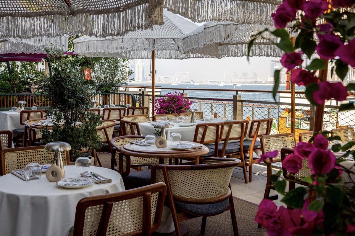 Miya Dubai, Bluewaters Island Chic outdoor dining area with woven chairs, fringe umbrellas, and vibrant flowers overlooking the water