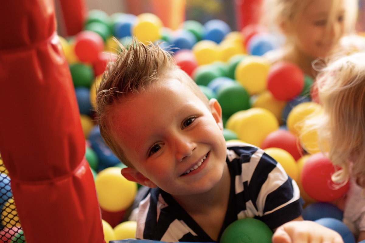 Privilee Gyms with Kids’ Clubs A joyful boy playing in a colorful ball pit, surrounded by bright red, yellow, and green balls.