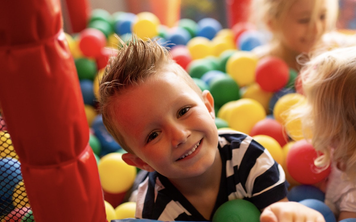 A joyful boy playing in a colorful ball pit, surrounded by bright red, yellow, and green balls.