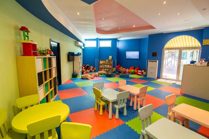Junior Jungle Kids’ Club, Habtoor Grand Resort Colorful indoor kids' playroom with tables, chairs, and foam floor tiles.
