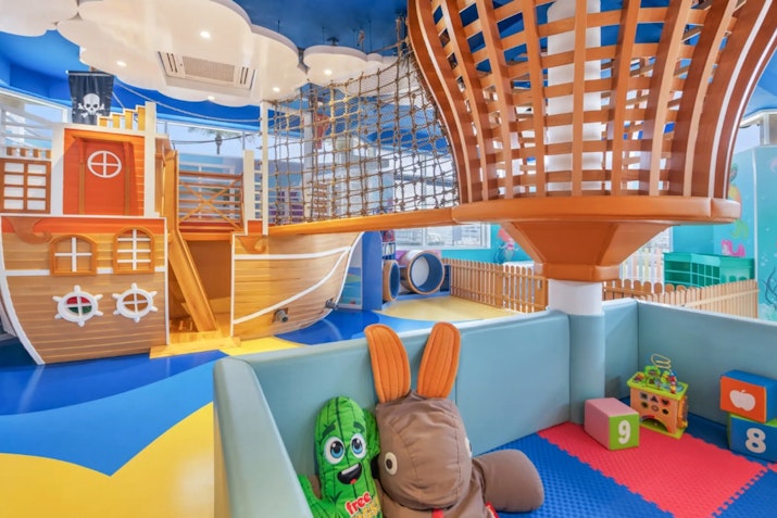 Children’s play area featuring a pirate ship play structure, soft toys, and colorful flooring
