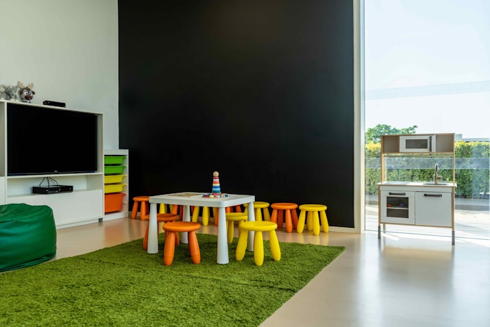 Colorful children's play area with yellow stools, a toy kitchen, and green carpet