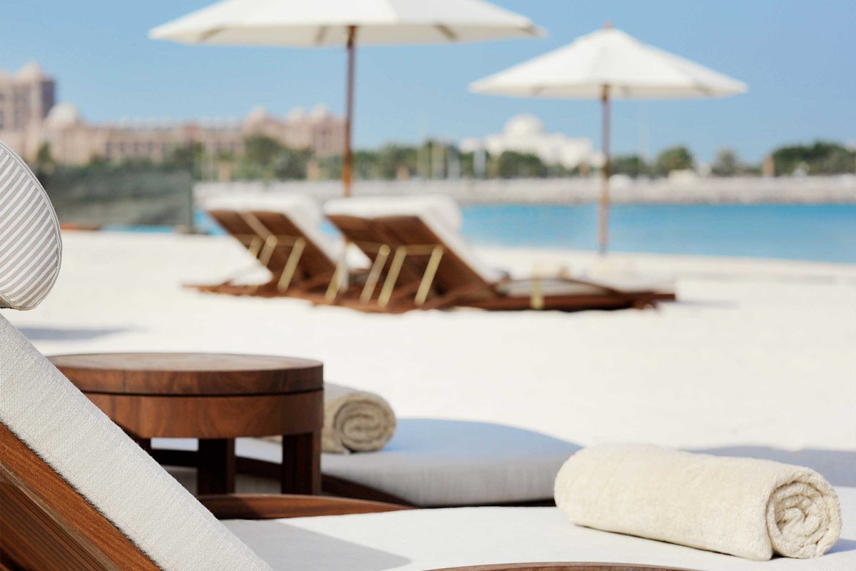 Beach lounge chairs with umbrellas on white sand overlooking the ocean