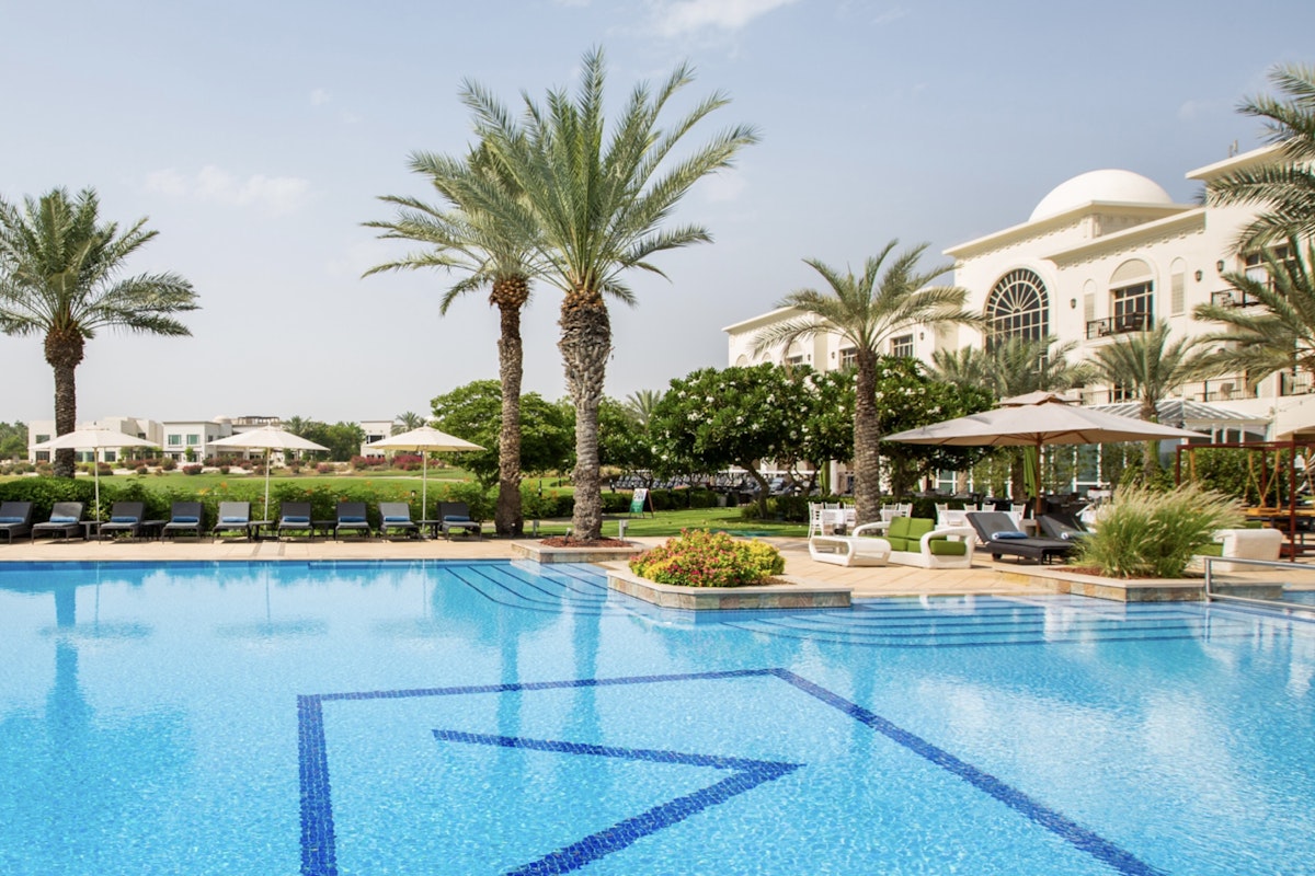 Address Montgomerie A poolside view with palm trees and lounge chairs, with a building in the background.