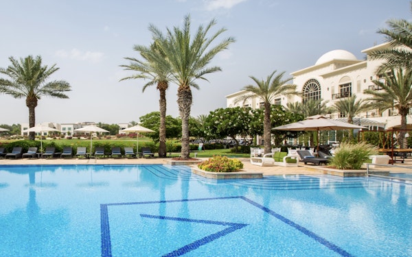 A poolside view with palm trees and lounge chairs, with a building in the background.