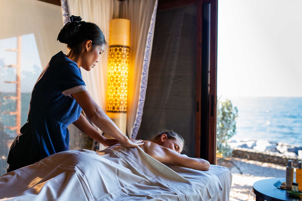 A spa therapist giving a massage to a woman by the beach.