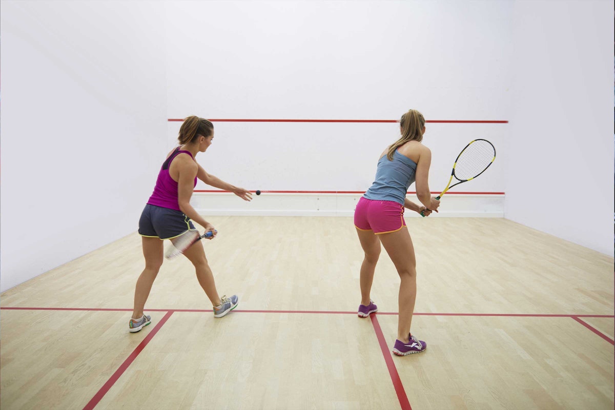 Two women playing squash in a sports hall.