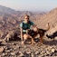 Privilee Team Spotlight Tom Man and dog posing on a mountain top with a scenic backdrop.