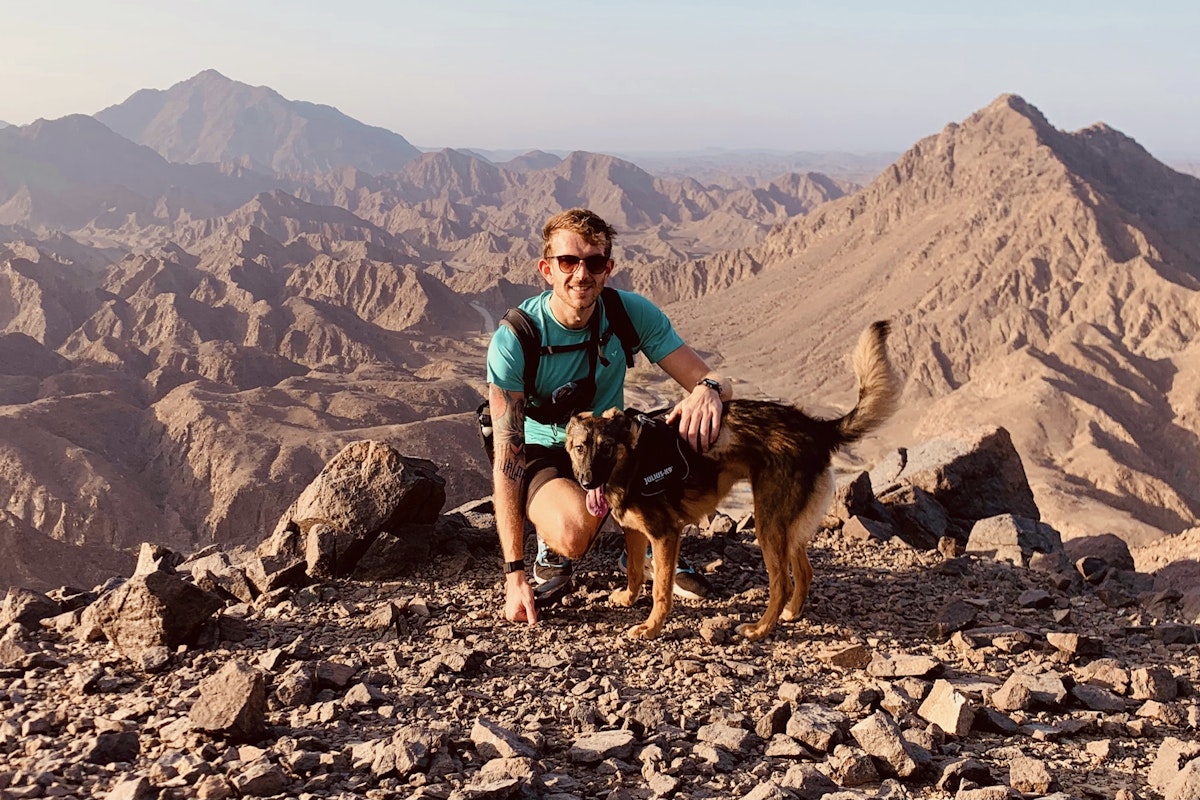 Privilee Team Spotlight Tom Man and dog posing on a mountain top with a scenic backdrop.
