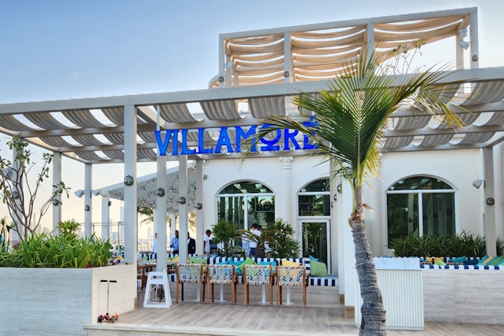 Exterior view of a restaurant named "Villamore" with outdoor seating and tropical landscaping.