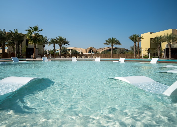 Asrah, Erth Abu Dhabi  Pool with loungers submerged in the water and palm trees in the background.