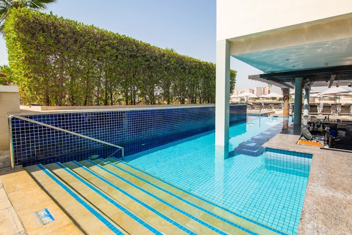 Swimming pool with stairs leading into the water, surrounded by greenery.