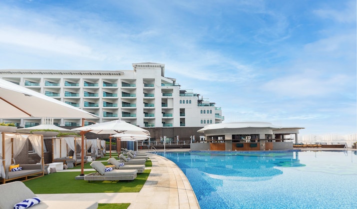 Infinity pool with lounge chairs and umbrellas, with a hotel in the background.