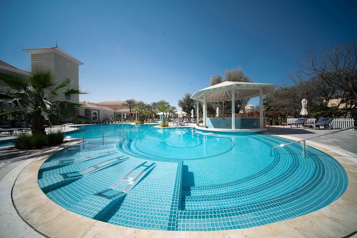 Circular pool with steps and a pavilion, surrounded by palm trees.       You said: