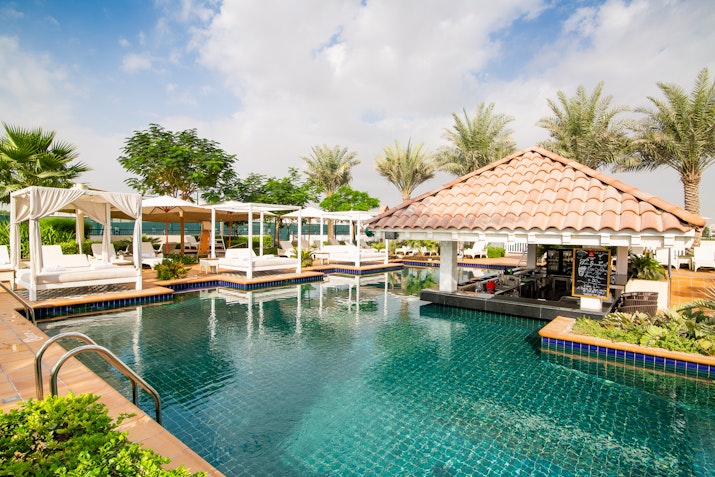 Pool with a thatched-roof cabana and lounge areas surrounded by palm trees