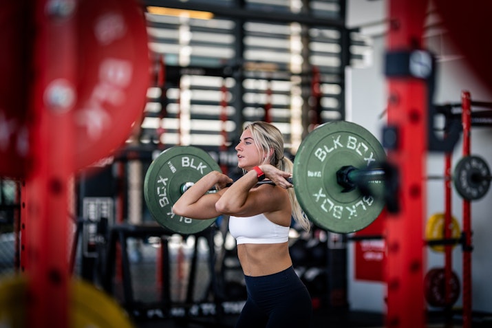 A woman performing a barbell squat in a gym, focusing on her form
