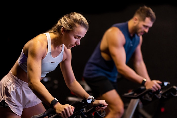 A man and woman participating in an indoor cycling class, focused on their workout