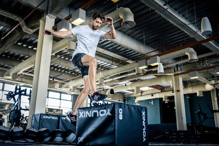 A male athlete performing a box jump on a workout platform in a well-equipped gym