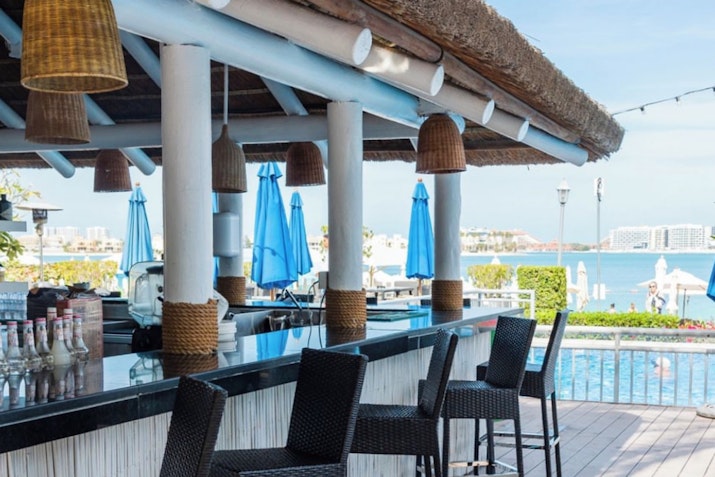 Outdoor bar with wicker stools, hanging lights, and a view of the pool and ocean.