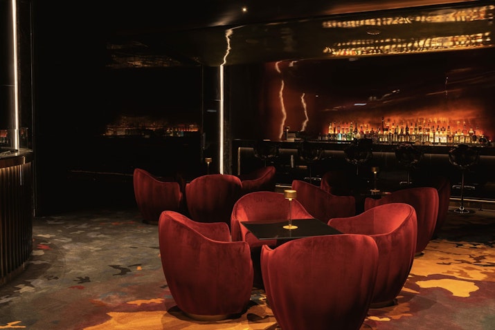 Elegant, dimly lit lounge with plush red chairs and a backlit bar area.