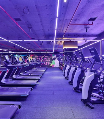 StudioRepublik A modern gym interior featuring several treadmills lined up under vibrant purple and pink neon lights.