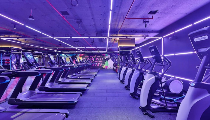 StudioRepublik A modern gym interior featuring several treadmills lined up under vibrant purple and pink neon lights.