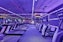 A modern gym interior featuring several treadmills lined up under vibrant purple and pink neon lights.