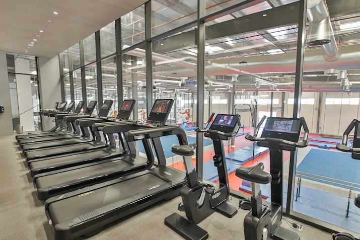 Modern gym equipped with advanced workout machines and weights overlooking a gymnastics floor