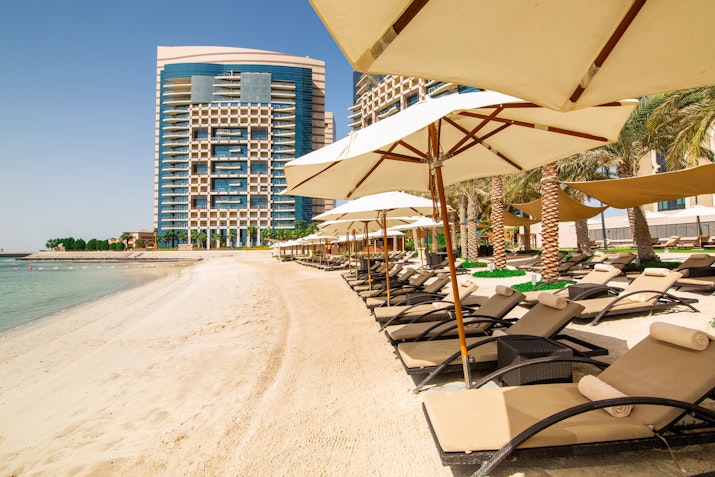 A beach with lounge chairs under umbrellas, and a tall building in the background.