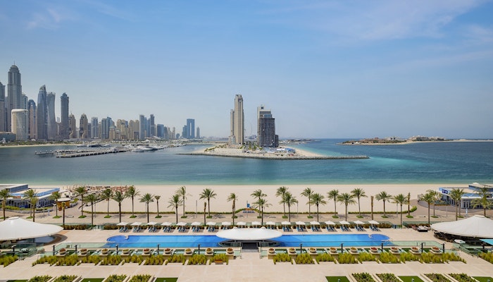 Hilton Dubai Palm Jumeirah A stunning view of the beach, pools, and palm trees with a city skyline in the background.