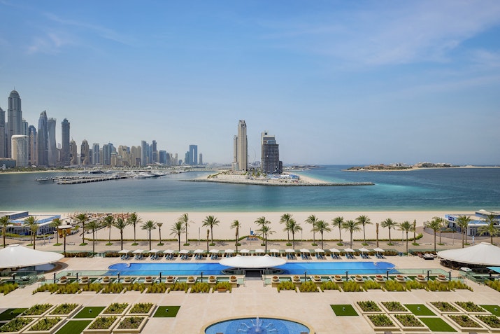 Hilton Dubai Palm Jumeirah A stunning view of the beach, pools, and palm trees with a city skyline in the background.