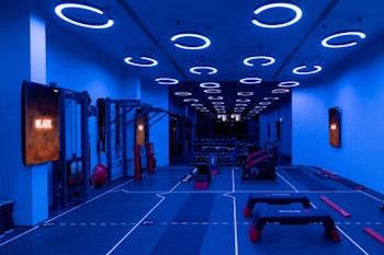 A modern gym interior illuminated with blue lights, featuring exercise equipment and a spacious workout area