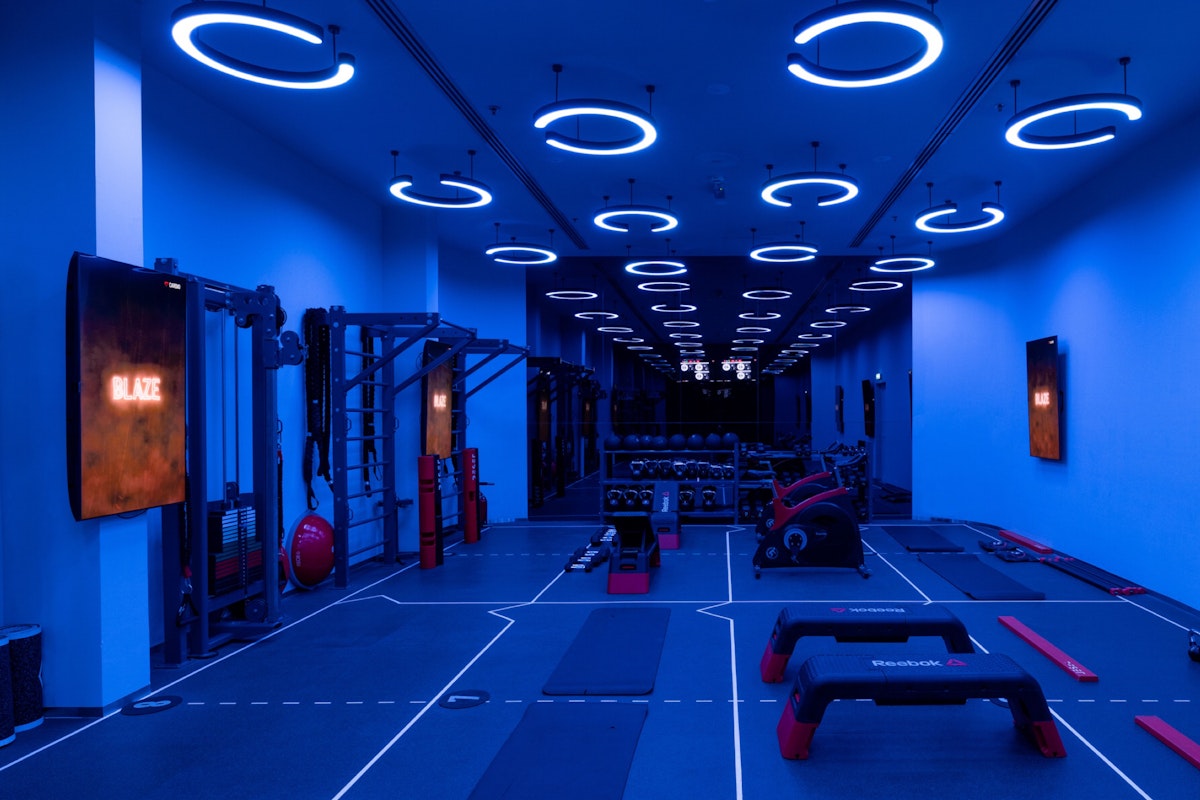 A modern gym interior illuminated with blue lights, featuring exercise equipment and a spacious workout area