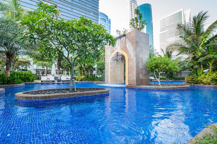 Outdoor pool with trees and an arch fountain feature.